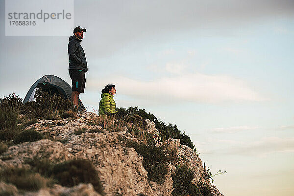 Frau und Mann sitzen auf der Klippe und blicken auf die Landschaft.