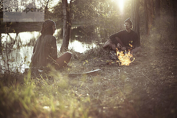 Freunde unterhalten sich am Feuer bei natürlichem Licht am Wasser