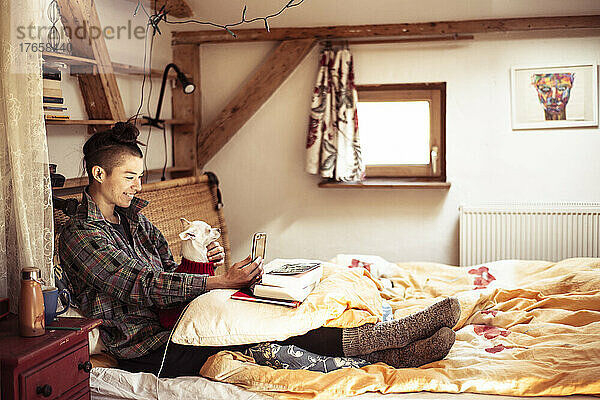 Frau mit gemischter Abstammung sitzt mit Hund im Bett und telefoniert per Video-Chat