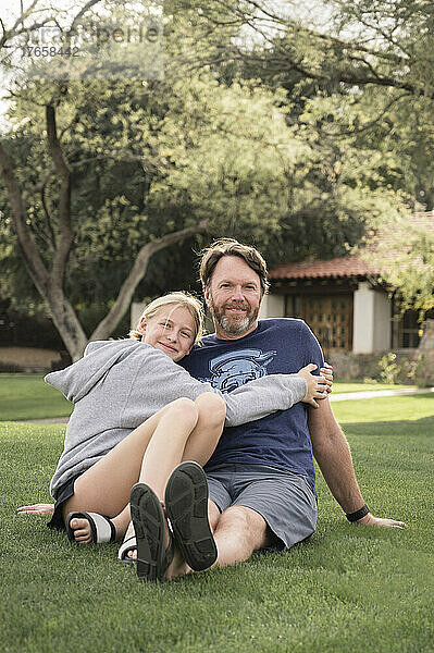 Vater und Teenager-Mädchen umarmen sich auf einem Rasen in Arizona