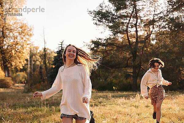 Zwei glückliche junge Frauen lächeln beim Laufen im Wald im Herbst