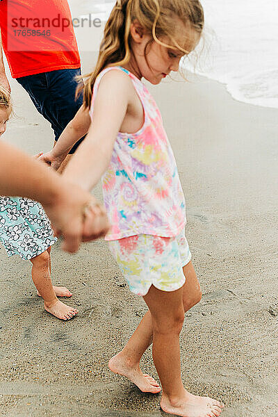Junges Mädchen hält Händchen mit ihrer Familie  während sie am Strand ist