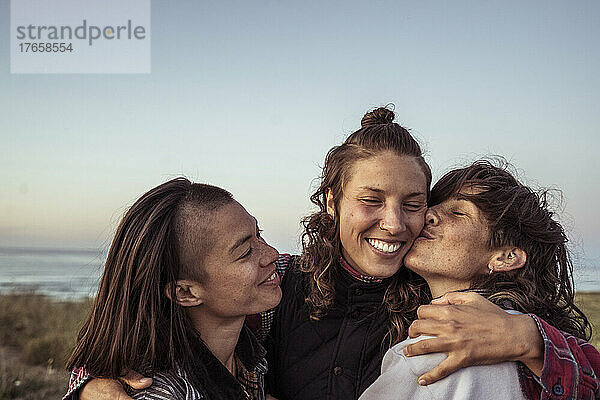 Queere alternative glückliche Gruppe von Frauen umarmen sich am Meer