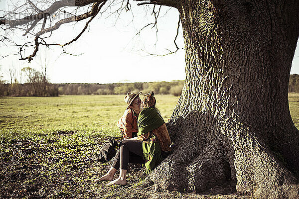 Romantisches androgynes Paar küsst sich unter einem großen Baum auf einer Wiese