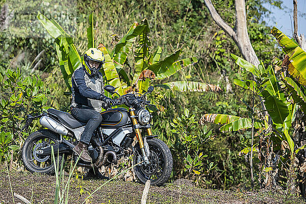 Mann mit seinem Scrambler-Motorrad auf unwegsamem Gelände in Thailand