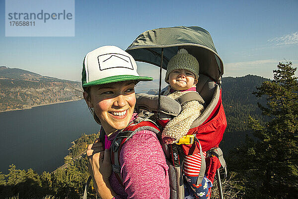 Eine junge Frau steht mit einem Baby im Rucksack auf einem Berg