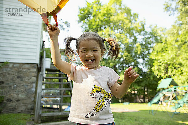 Glückliches kleines Kind lächelt  während es im Hinterhof einen Fallschirm hält