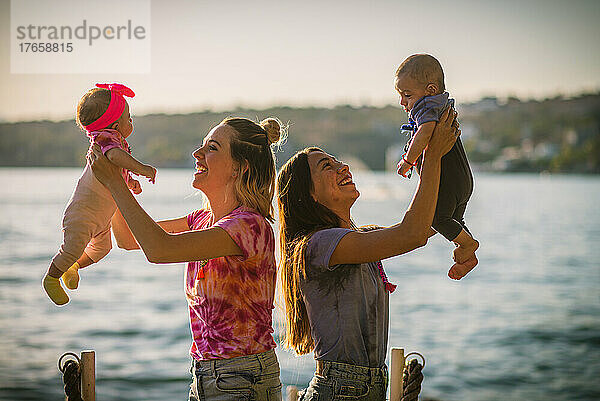 Zwei Mütter spielen mit ihren Babys an einem sonnigen Nachmittag am See