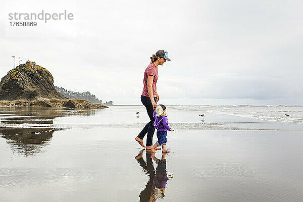 Eine junge Frau geht mit einem kleinen Kind an einem riesigen  leeren Strand spazieren