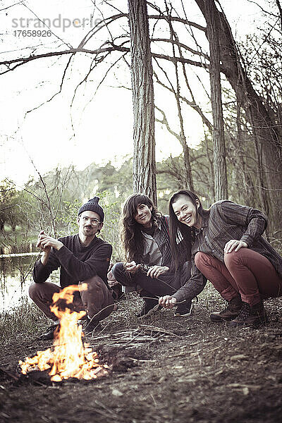 Freunde posieren vor Feuer am Fluss und an Bäumen