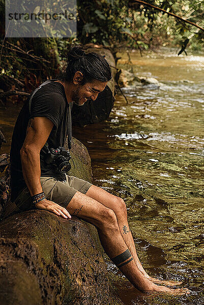 Mann sitzt auf einem Baum mit seinen Füßen auf dem Fluss