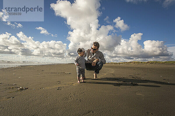 Ein Mann kauert an einem breiten  leeren Strand  um mit einem Kleinkind zu sprechen