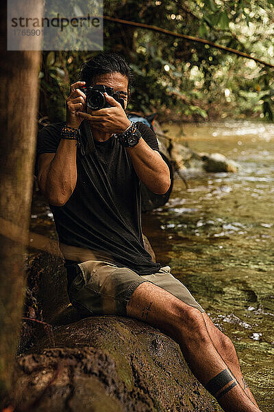 Mann sitzt auf einem Baum und fotografiert mit seiner professionellen Kamera