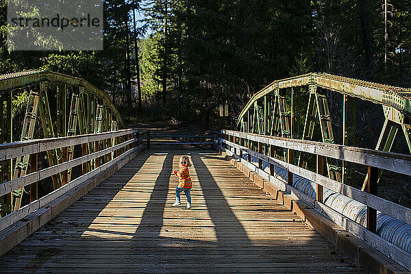 Ein junges Mädchen rennt im Sonnenschein über eine alte Holzbrücke