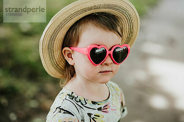Nahaufnahme eines Kleinkindes  das draußen eine herzförmige Sonnenbrille trägt