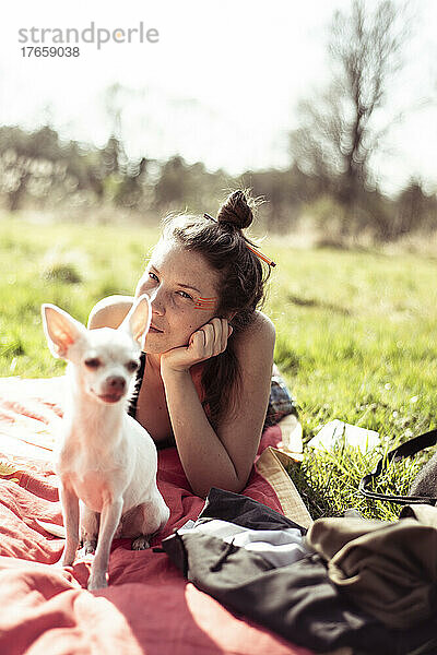 Schöne Frau mit kleinen Chihuahua liegt in der Sonne auf Gras in der Natur