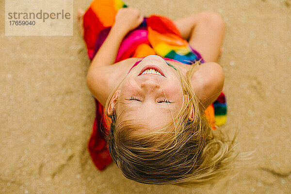 Siebenjähriges Mädchen lächelt am Strand im Regenbogenkleid