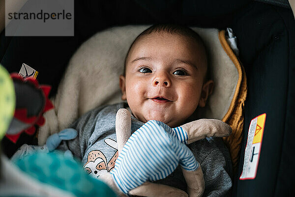 Baby liegt im Kinderwagen. Lächelnd neben ihrem Teddybären.