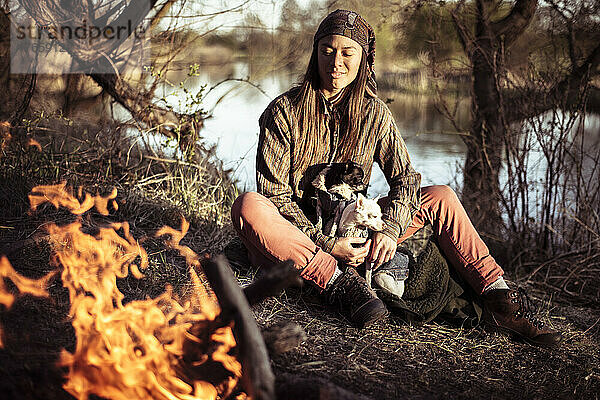 Mischlingsmensch in der Nachmittagssonne bei Wasser und Feuer mit kleinen Hunden