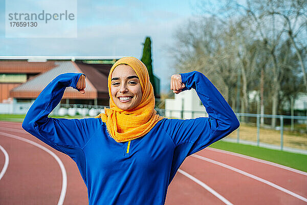 Fröhliche muslimische Frau zeigt Handmuskeln auf dem richtigen Weg