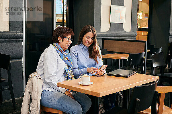 Reife Frau und junge Frau schauen in einem Café auf ein Mobiltelefon