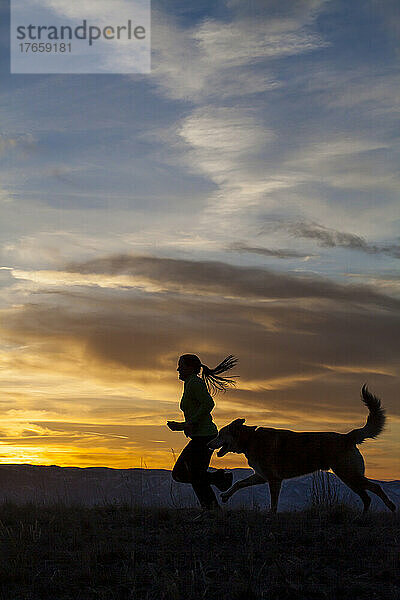 Eine Frau läuft bei Sonnenuntergang mit einem Hund auf einem Pfad.