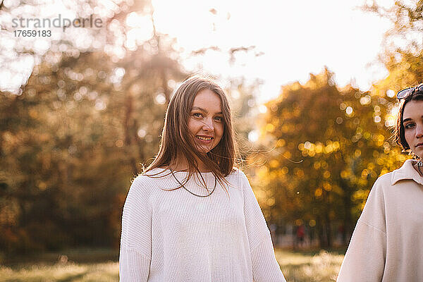 Porträt einer glücklichen jungen Frau  die mit ihrer Freundin im Park steht