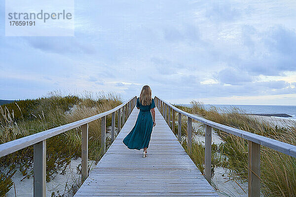 Elegantes Mädchen  das einen Gehweg vor dem Meer entlang geht