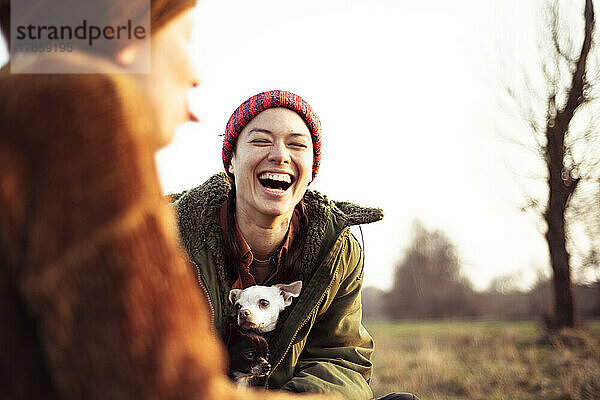 Zwei Freunde lachen über Witze mit Hunden beim Picknick in der Wintersonne auf dem Feld