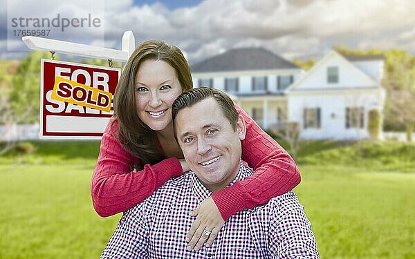 Glückliches Paar vor einem verkauften Immobilienschild und einem schönen Haus