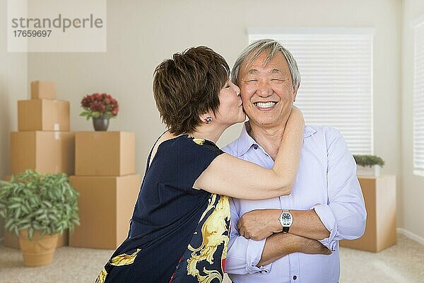 Glückliches älteres chinesisches Paar in einem leeren Raum mit Umzugskartons und Pflanzen
