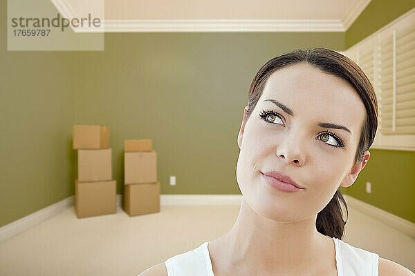 Attraktive tagträumende junge Frau im leeren grünen Raum mit Kisten