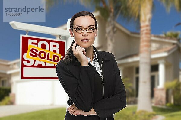 Attraktive gemischtrassige Frau vor einem Haus und einem Schild mit verkauften Immobilien
