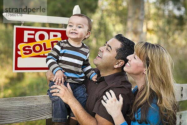 Glückliches gemischtrassiges Paar mit Baby vor einem Schild mit verkauften Immobilien