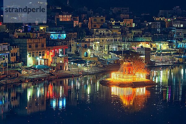 View of famous indian hinduism pilgrimage town sacred holy hindu religious city Pushkar with Brahma temple  aarti ceremony  lake and ghats illuminated at sunset. Rajasthan  India. Horizontal pan