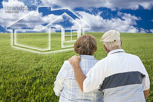 Loving senior couple standing in graß field looking over at ghosted house on the horizon