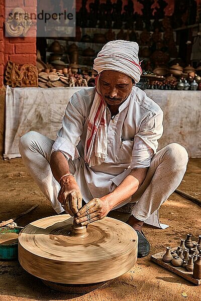 Indian potter at work: throwing the potter's wheel and shaping ceramic vessel and clay ware: pot  jar in pottery workshop. Experienced master. Handwork craft from Shilpagram  Udaipur  Rajasthan  India