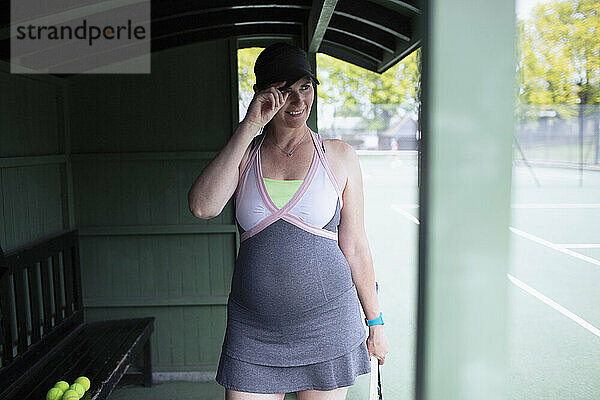 Lächelnde schwangere Frau im Kleid auf dem Tennisplatz