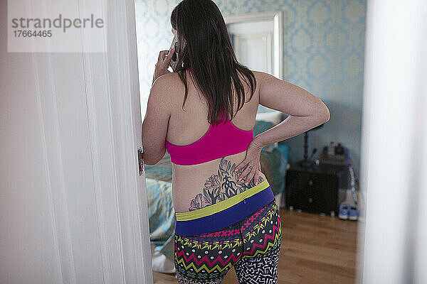 Schwangere Frau im Sport-BH mit Tattoo  die mit ihrem Smartphone telefoniert