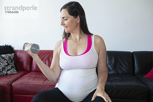 Schwangere Frau trainiert mit Hantel zu Hause