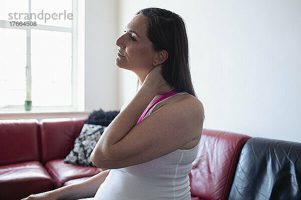 Schwangere Frau reibt sich den Nacken auf dem Sofa