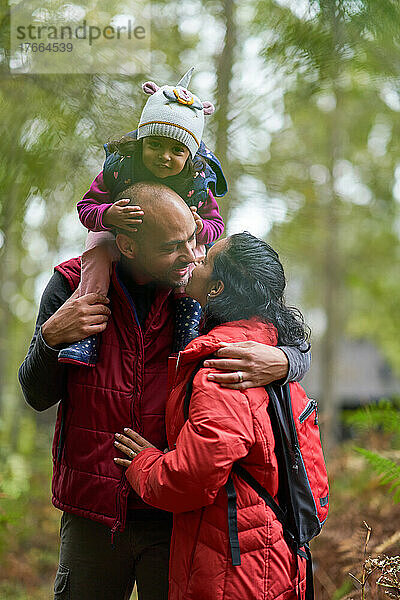 Zärtliches Paar mit kleiner Tochter küsst sich beim Wandern
