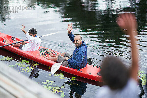 Glücklicher Vater und Sohn winken vom Kajak aus auf dem Fluss