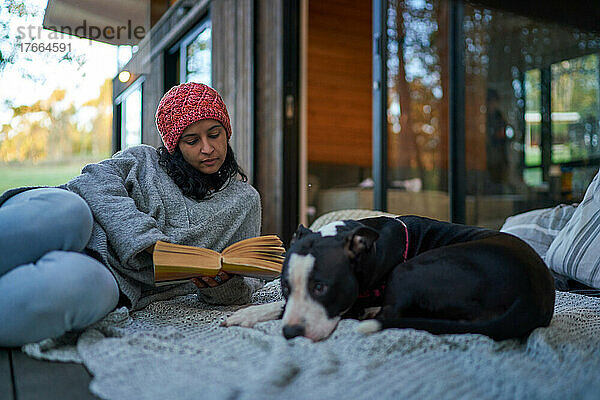 Eine Frau liest ein Buch neben ihrem Hund auf der Terrasse eines Ferienhauses