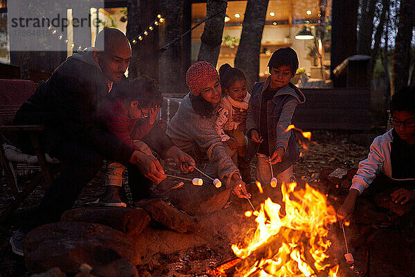 Familie toastet Marshmallows am Lagerfeuer vor der Hütte