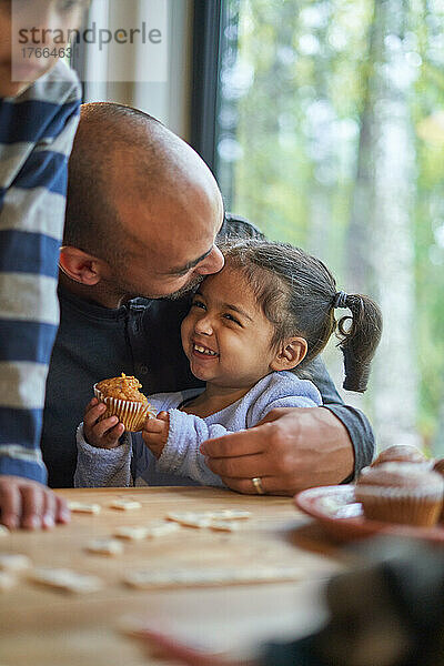 Vater umarmt glückliches Kleinkind Tochter essen Muffin am Tisch