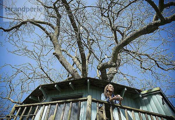 Junge Frau trinkt Kaffee auf dem sonnigen Balkon eines Baumhauses