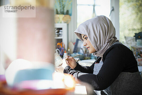 Fokussierte junge Künstlerin im Hidschab  die im Kunstatelier Keramik malt