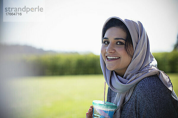 Porträt einer glücklichen jungen Muslimin im Hidschab  die Saft trinkt