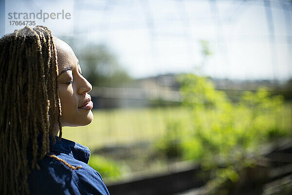 Gelassene junge Frau mit geschlossenen Augen im sonnigen Garten